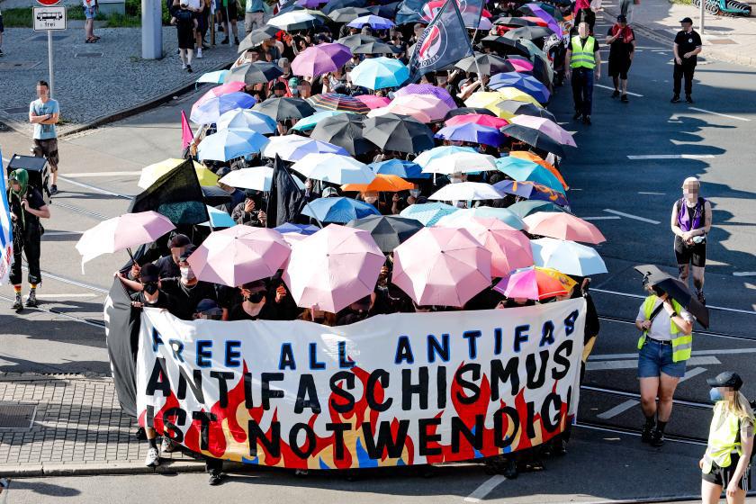 Demozug von vorne mit vielen bunten Regenschirmen und Frontbanner: "Free All Antifas. Antifaschismus ist notwendig" und bunten Flammen
